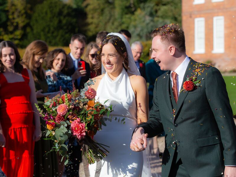 Ellie and Jack walking through confetti with Ellie’s autumn bouquet and Jack’s buttonhole