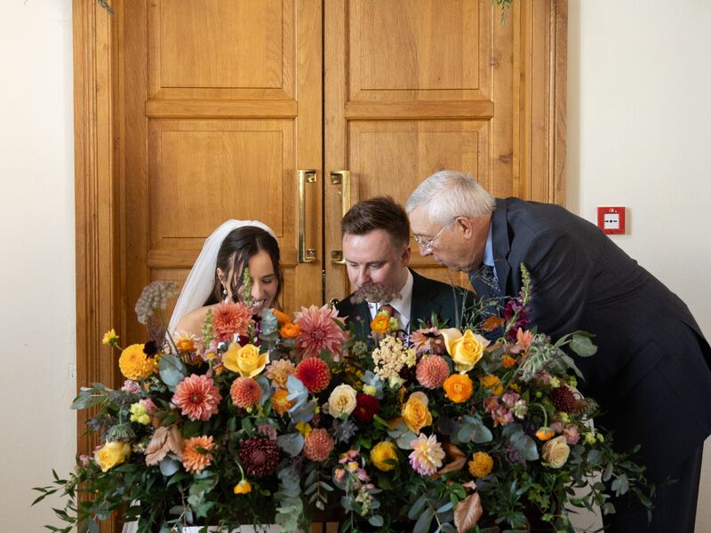 Ellie and Jack signing the register behind a colourful autumn altar arrangement