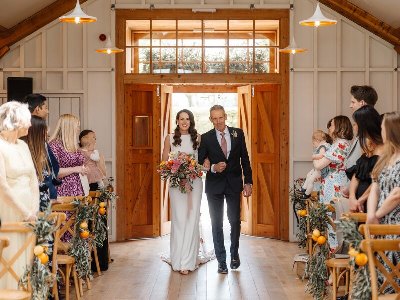 Holly walking through the Hyde House ceremony room with citrus and olive aisle flowers