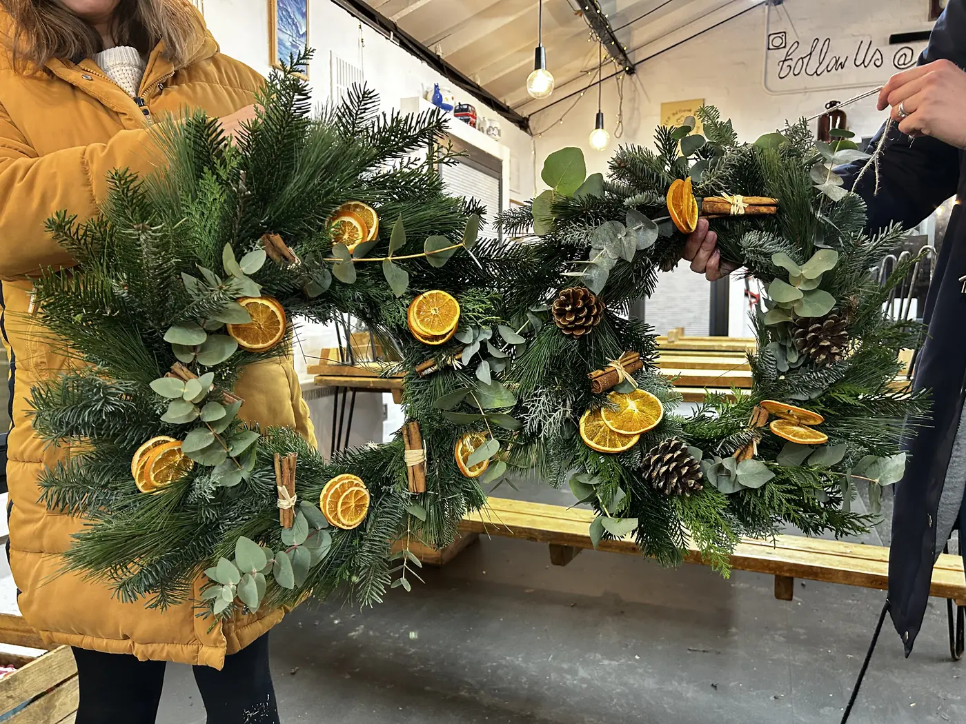 Two finished evergreen Christmas wreaths decorated with dried citrus and pine cones