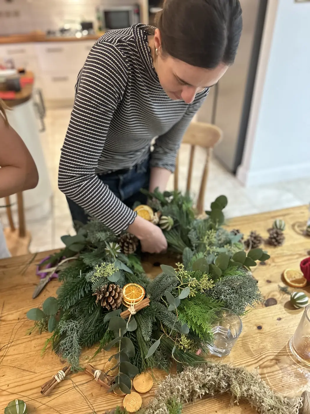 Guest decorating a natural Christmas wreath with foliage and dried orange